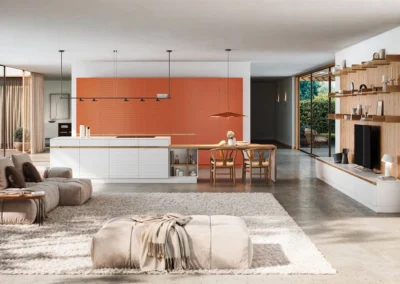 Cocina abierta blanca y terracota con isla, mesa integrada y mueble de salón coordinado con estanterías de madera