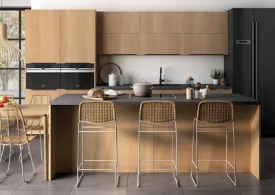 Cocina de madera clara con isla y barra de desayuno, encimera de piedra oscura, taburetes de ratán y horno doble Siemens