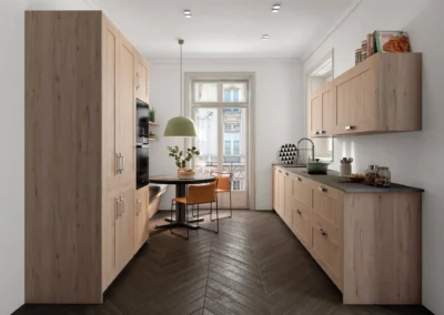 Cocina de madera clara estilo nórdico en paralelo con encimera gris, horno columna empotrado y mesa redonda con sillas naranjas