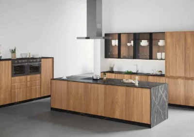 Cocina de madera nogal y gris con isla de mármol blanco, muebles columna con horno doble Siemens y vitrinas iluminadas